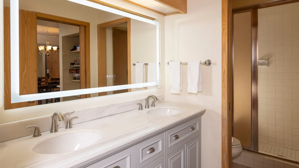 A well-appointed bathroom featuring a double sink, a backlit mirror, fresh towels, and a modern shower area. The space exudes a sense of freshness and calm, ideal for morning routines or evening self-care rituals.