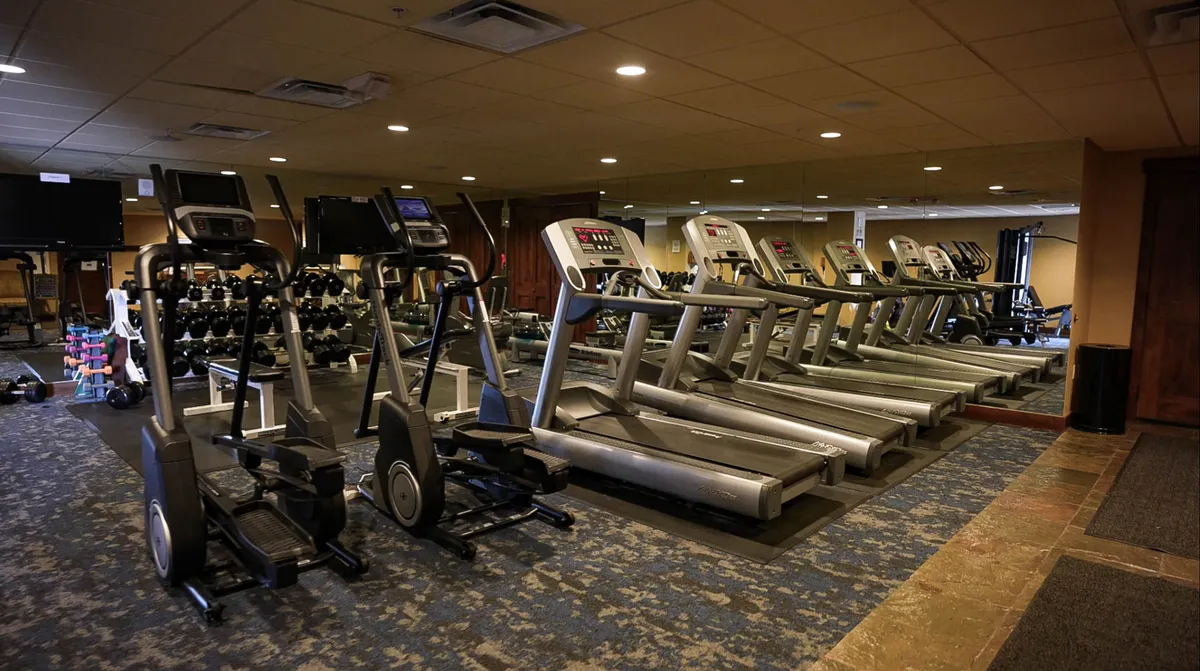 A modern fitness center featuring ellipticals, treadmills, dumbbells, and mirrored walls. The space is filled with natural light and exudes energy, offering everything needed for a post-hike workout or pre-adventure warm-up.