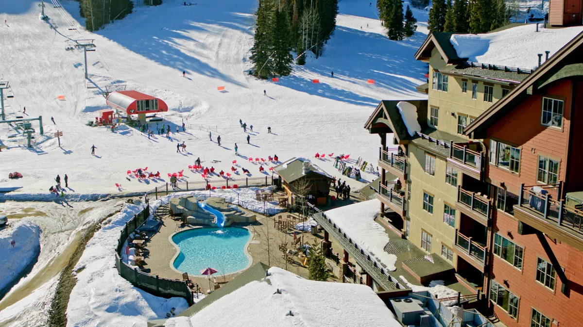 An exterior view of the lodge with a swimming pool and ski slopes in the background. People are seen skiing, swimming, and relaxing by the pool, capturing the lively atmosphere of resort life and the unique combination of adventure and relaxation.