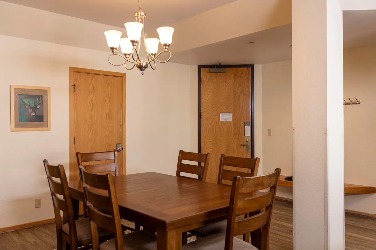 A warm dining area centered on a large wooden dining table under a stylish chandelier. Framed artwork and soft lighting create an inviting setting for family dinners, festive gatherings, or a quick bite before hitting the slopes. The table is positioned to encourage conversation and connection.