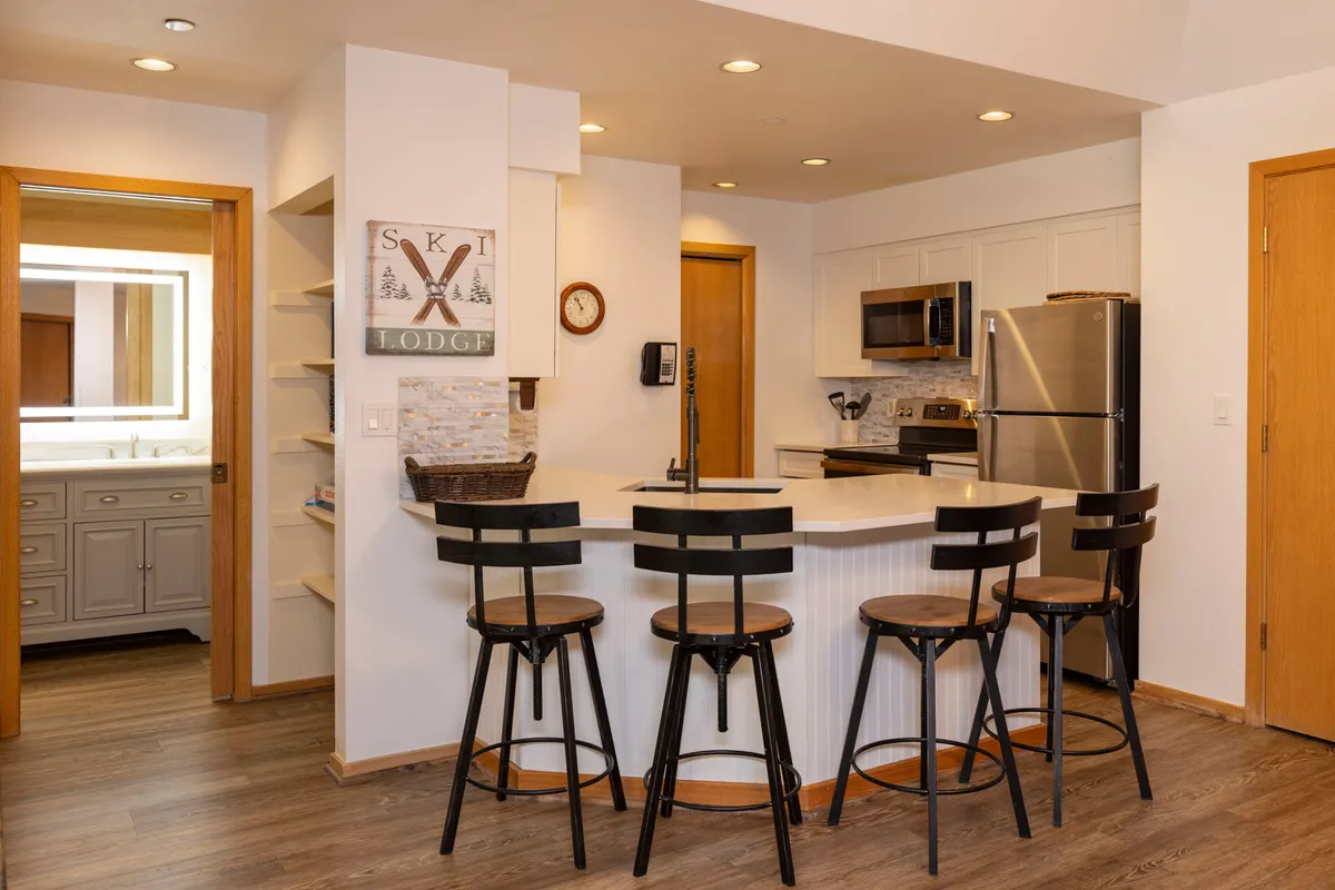 A modern kitchen space featuring a kitchen island with seating, the prominent 'SKI LODGE' sign, and gleaming modern appliances. The setting is bright and welcoming, designed for socializing and preparing meals. The island doubles as a spot to enjoy casual breakfasts or après-ski snacks, with ample counter space for cooking.
