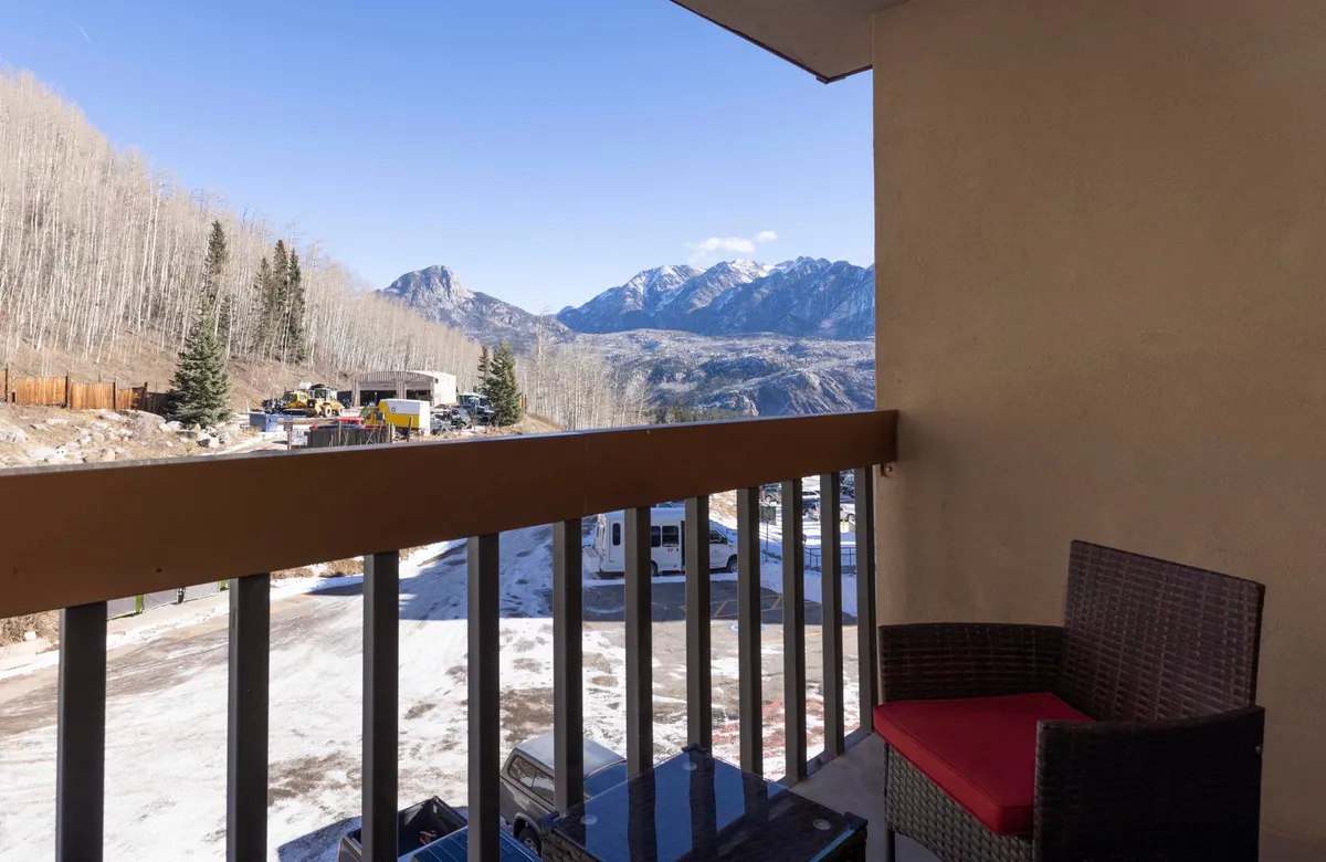 A tranquil exterior scene showing a balcony with comfortable seating surrounded by aspen trees, overlooking a breathtaking mountain view. The golden hour light highlights the natural tranquility, inviting relaxation and appreciation of the surrounding landscape.